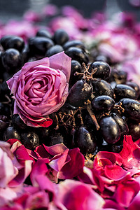 玫瑰花黑色摄影照片_黑色木板上一串生鲜葡萄的特写镜头，上面有一些红色和粉红色的玫瑰花。