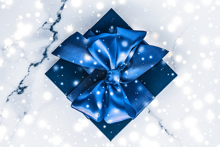圣诞广告摄影照片_冬季节日礼盒，配有蓝色丝绸蝴蝶结、大理石背景上的雪花，作为豪华美容品牌的圣诞和新年礼物，平铺设计