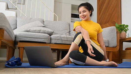 微笑的亚洲女人在家里的垫子上练习瑜伽。