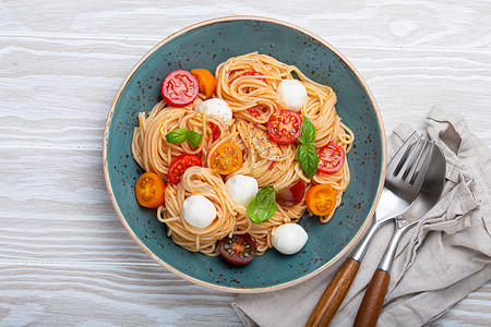 意大利面条配马苏里拉奶酪、彩色樱桃番茄、陶瓷盘上的新鲜罗勒