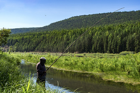 渔夫站在河里，用木鱼竿钓鱼。