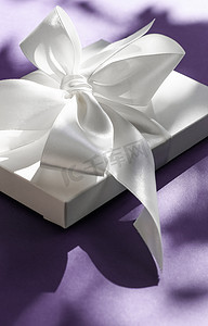 紫罗兰色背景上带丝带和蝴蝶结的豪华假日白色礼盒、豪华婚礼或生日礼物