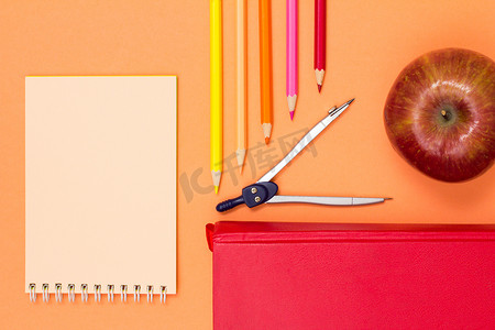 粉色背景上的笔记本、书籍、指南针、彩色铅笔和苹果