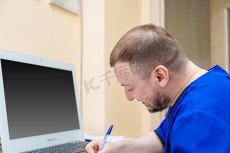 一位男性眼科医生坐在电脑前的工作场所，用笔写字