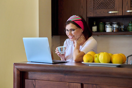在家休息摄影照片_40 多岁的女性在家休息，喝着咖啡，看着笔记本电脑