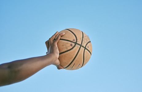 篮球、活跃和运动员手握球，从下方以蓝天背景展示胜利、力量或运动健康。