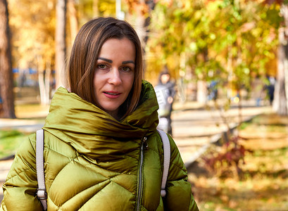 色彩缤纷的金色秋叶中穿着绿色夹克的迷人年轻女子