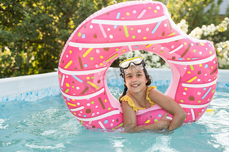 炎热的夏日，快乐的小女孩在室外游泳池里玩彩色充气环。