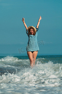 海边水花摄影照片_夏天海边的一个美丽女孩高兴地在水上玩耍，情绪激动