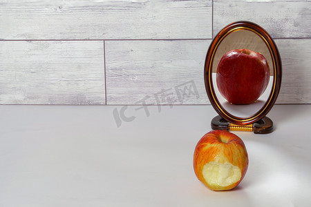 镜子现实摄影照片_被咬过的红苹果映在镜子里。