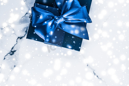 蓝色品牌展示摄影照片_冬季节日礼盒，配有蓝色丝绸蝴蝶结、大理石背景上的雪花，作为豪华美容品牌的圣诞和新年礼物，平铺设计