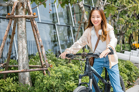 快乐的太阳摄影照片_快乐的亚洲美丽年轻女子在建筑城市附近的户外街道上骑自行车