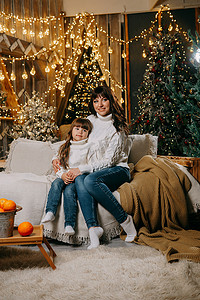一个小女孩和她的母亲在圣诞树旁边的沙发上享受舒适的家庭环境。