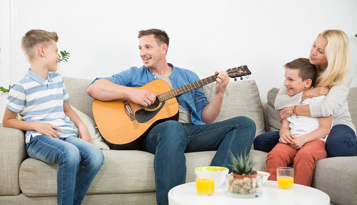 快乐的白人家庭在舒适的现代家里微笑、弹吉他、唱歌