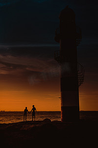 剪影灯塔摄影照片_一对夫妇的剪影和一座巨大的灯塔。