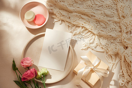 浅色背景下的空白纸条、牛皮纸信封、礼品盒、织物和鲜花的顶视图