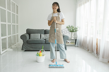 洗衣摄影照片_年轻女子在家用拖把清洁地板。
