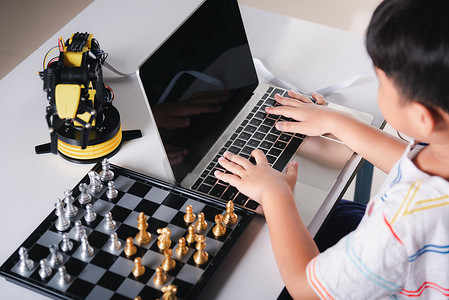 亚洲小男孩在笔记本电脑上为机器人机械臂编程代码以下棋