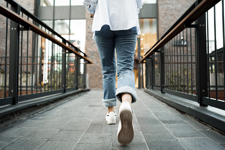 一个穿着牛仔裤和运动鞋的女人在街上行走的后视图