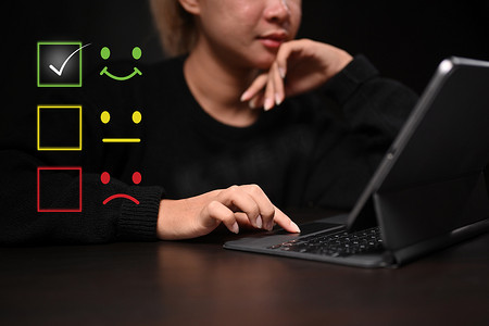 年轻女性使用电脑平板电脑选择笑脸图标来评估产品和服务。