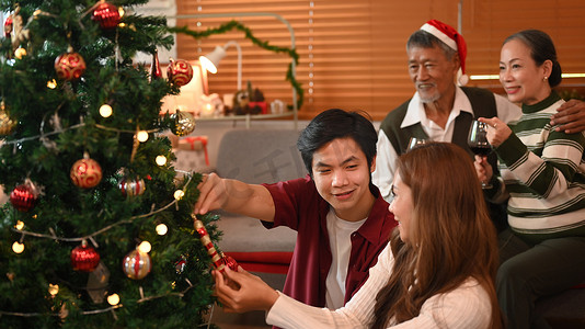 欢庆庆祝摄影照片_恩爱的年轻夫妇装饰圣诞树，准备在舒适的客厅里一起庆祝寒假