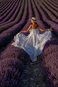 迷人的年轻女子，戴着帽子，穿着白色的裙子，在紫色的薰衣草田里。