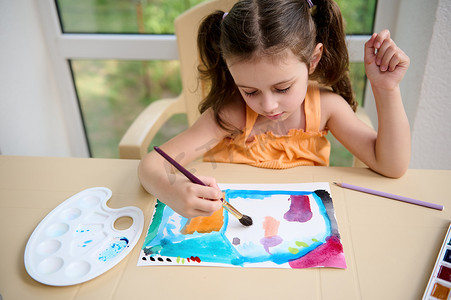 二年级语文摄影照片_从上面看，一个白人快乐的小女孩用画笔和水彩画了一幅美丽的图画