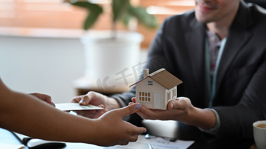 男性房地产经纪人持有房屋模型的裁剪图像并向客户提出建议。