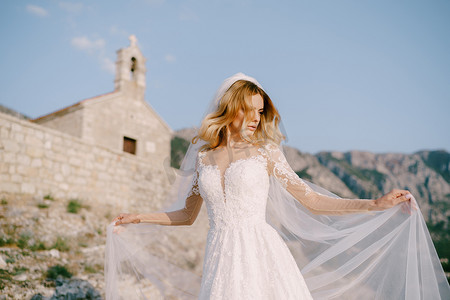 身穿白色蕾丝连衣裙的新娘站在一座古老石教堂的背景下