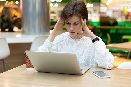 女自由职业者坐在商场的桌子旁，悬疑地看着笔记本电脑