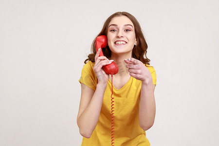 穿着黄色 T 恤的年轻漂亮女人微笑着指着你手里拿着固定电话，等待你的电话。