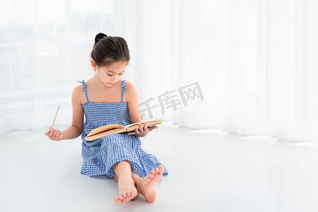可爱的女孩在家里的白色卧室背景下，手里拿着笔记本和木铅笔复习作业和课程。
