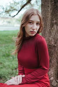 一个红衣女孩坐在春天森林的一棵树下，享受大自然