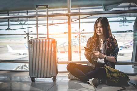 坐飞机摄影照片_亚洲女性旅客使用智能手机在机场检查航班时刻表。
