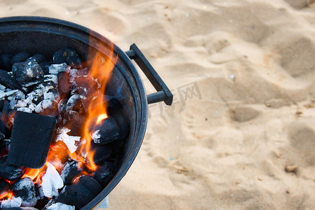 沙滩上圆形金属烧烤中燃烧着黄色火焰的木炭的特写