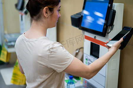 一位女士在商店的自助结账柜台用智能手机付款。