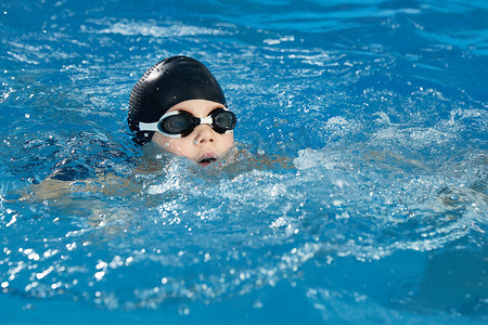 学龄前男孩学习如何戴着泳帽和护目镜在游泳池里游泳