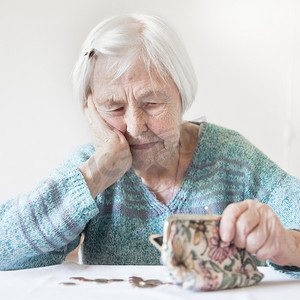 贫困老人摄影照片_坐在桌旁忧心忡忡的老妇人数着钱包里的钱。
