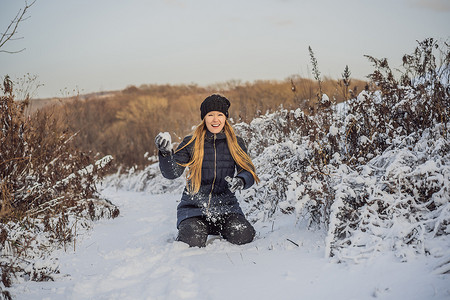 冬季女孩向相机扔雪球，微笑着快乐地在下雪的冬日在雪地里玩耍时在户外玩得开心。