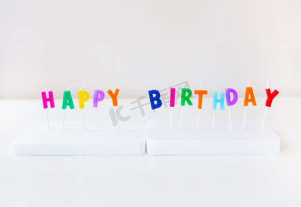 生日快乐庆祝蛋糕摄影照片_五颜六色的蜡烛与孤立在白色背景上的题字生日快乐。