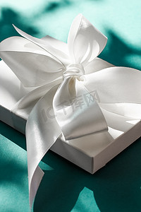 装饰礼物盒摄影照片_翠绿背景上带丝带和蝴蝶结的豪华假日白色礼盒、豪华婚礼或生日礼物