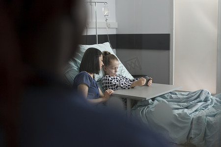 爱心app摄影照片_有爱心的父母坐在住院的生病女儿旁边，用智能手机观看动画片