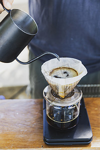咖啡师将热水从不锈钢茶壶中溢出，准备过滤咖啡，滴在黑色简单重量的造纸机上。
