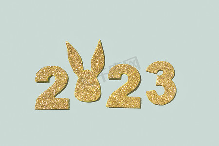 兔子新年快乐摄影照片_闪亮的金色数字 2023 年，兔耳象征新年，柔和的绿色背景
