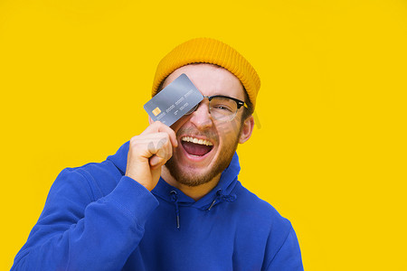 花钱买快乐摄影照片_快乐的年轻白人男子手里拿着信用卡、借记卡，微笑着遮住眼睛，准备花钱。