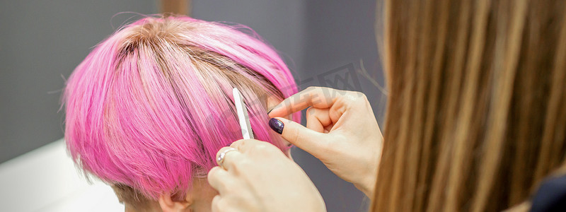 美发师正在为一位年轻女子染上粉红色的短发，准备在美容院进行手术。