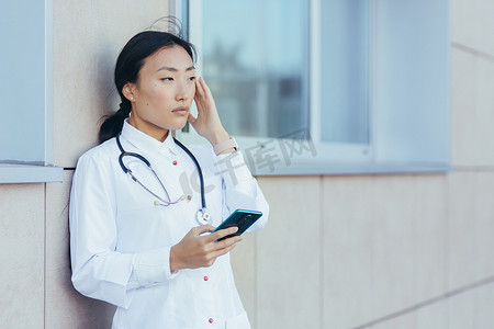 悲伤的亚洲医生护士，在休息时在诊所附近使用电话，女人严重头痛