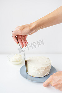 美味的奶油蛋糕，女孩用抹刀将鲜奶油涂在鲜奶油上，蛋糕就准备好装饰了。