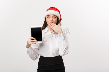 企业概念-圣诞节主题的年轻白种人女商人展示数字平板电脑与令人惊讶的面部表情。
