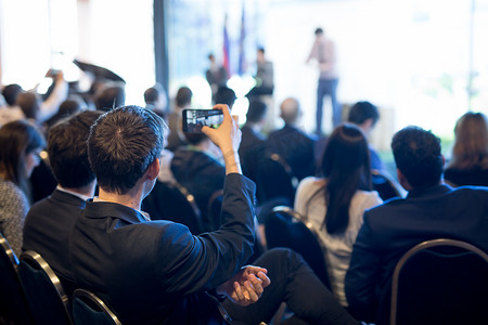商人使用智能手机在会议厅拍摄企业业务演示的照片。